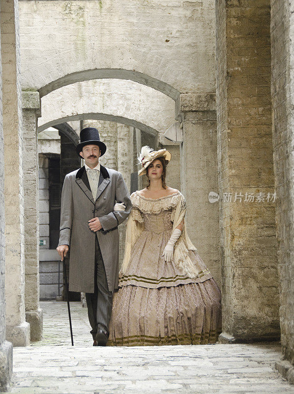 一对穿着维多利亚时代服装的夫妇走过石头走廊