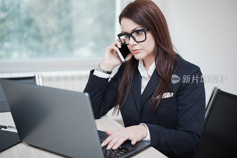 一位女商人一边在笔记本电脑上打字，一边打电话