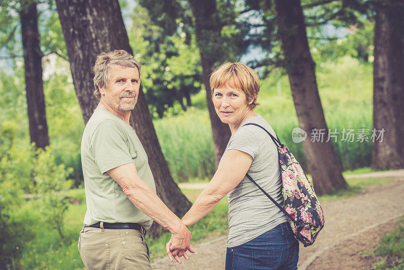 一对老年白种夫妇在户外散步，手牵着手，回头看