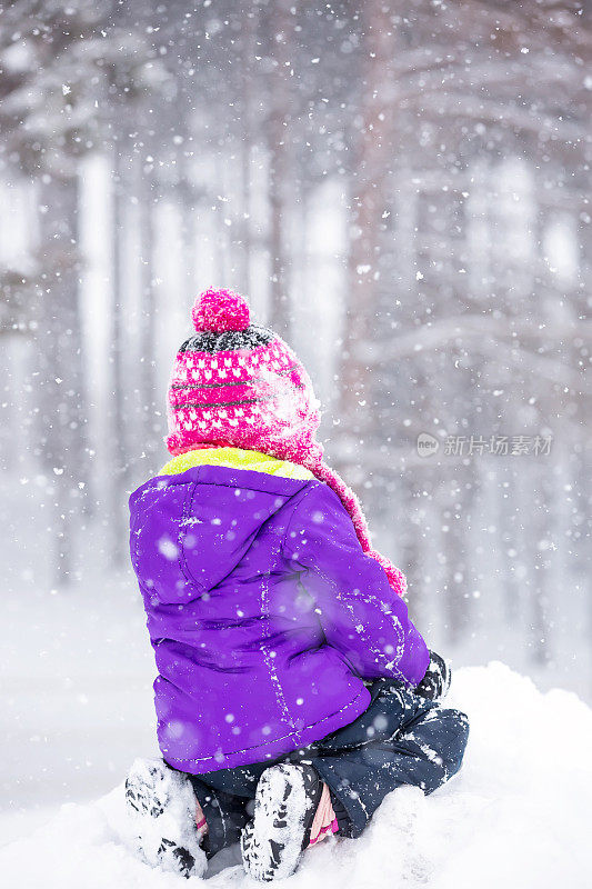 年轻女孩坐在雪堆上在冬季暴风雪