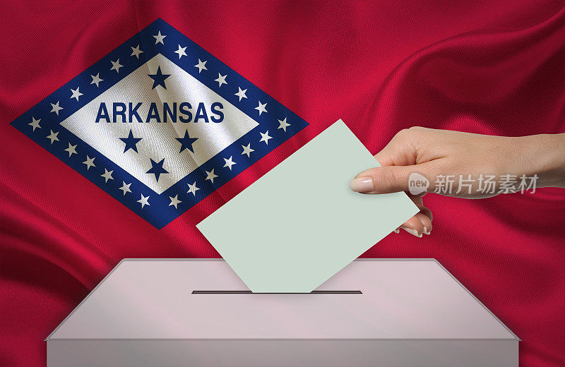手与投票选票和箱子在旗帜前阿肯色州-美国