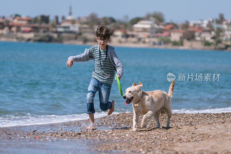 快乐的男孩和她的狗在沙滩上奔跑。