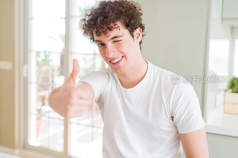 年轻英俊的男子穿着白色t恤做快乐的拇指手势与手。赞许的表情看着镜头，表示成功。