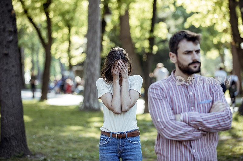 一对年轻夫妇在公园里吵架。年轻夫妇有一个夏天的一天争吵。站在公园外面，困惑的年轻女子打着手势，看着她的男朋友