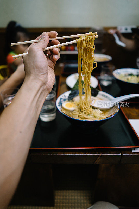 一个男人用筷子夹着面条在他面前
