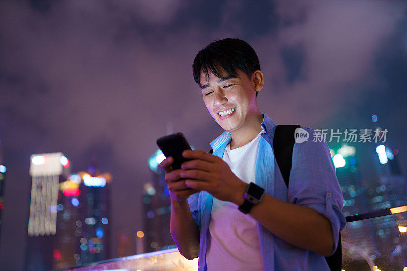 年轻的亚洲男子在晚上使用智能手机