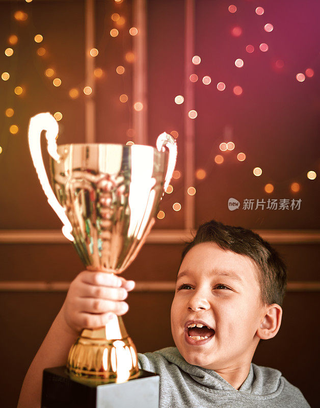 可爱的孩子拿着金杯。他是赢家。