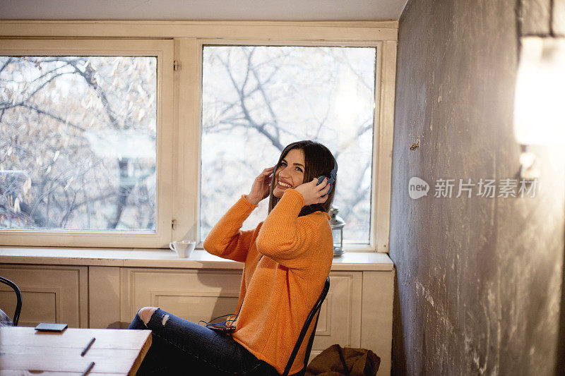 年轻漂亮的女人在窗边喝咖啡，戴着耳机听音乐
