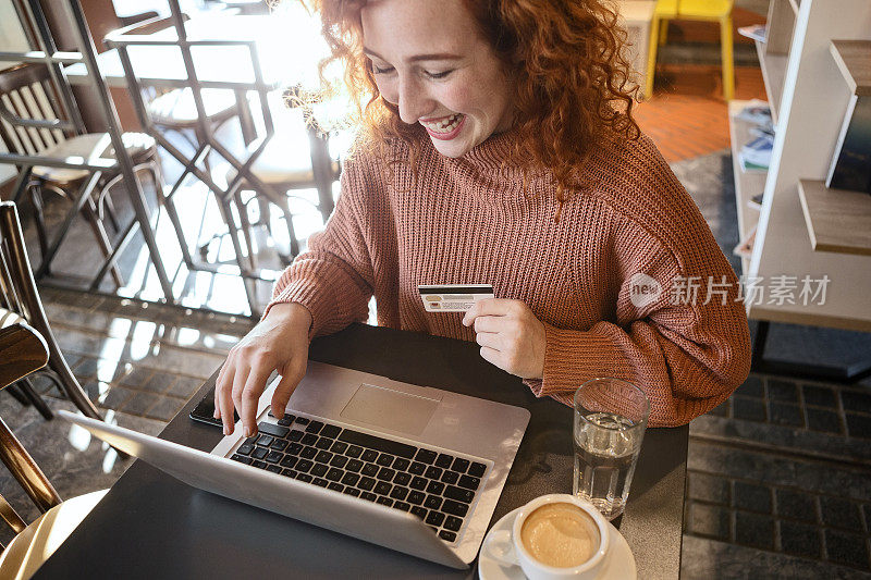 卷毛微笑红头发的女人正在考虑进行网上信用卡购买
