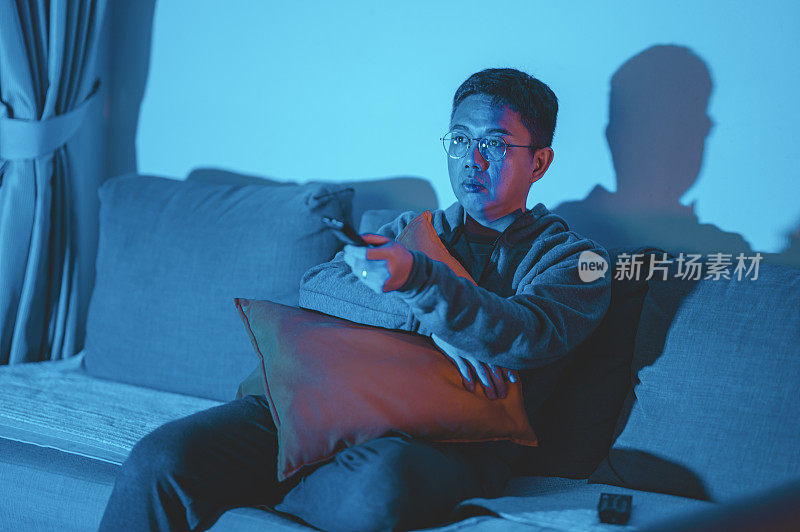 一个亚洲华人中年人在黑暗中独自在家看电影