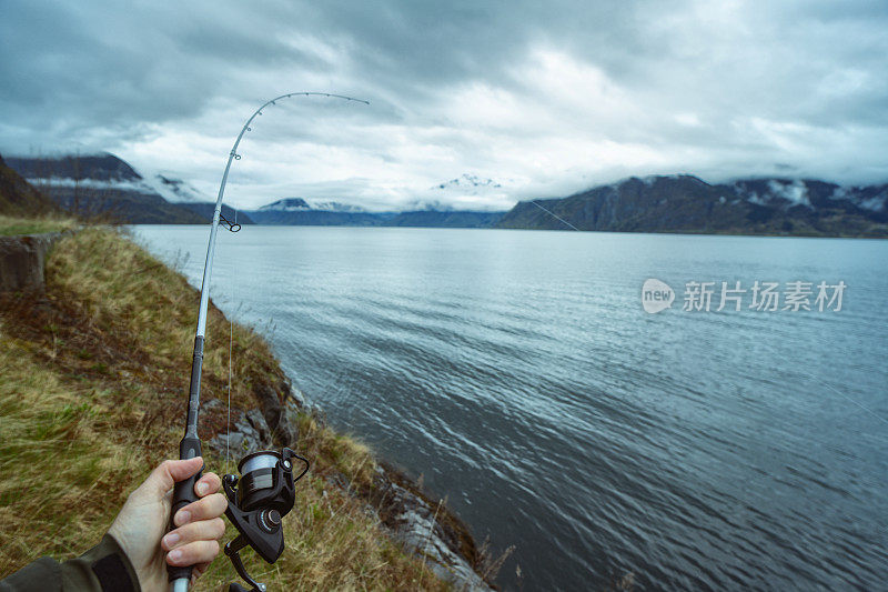 一名男子在挪威峡湾边用鱼竿在海里钓鱼