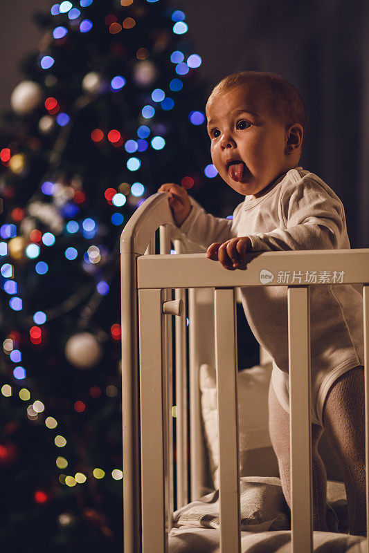快乐的小女孩站在她的婴儿床在圣诞节的晚上和玩