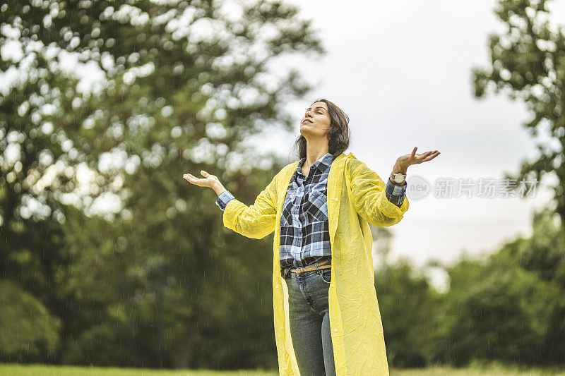 快乐的年轻女子穿着黄色雨衣，享受着雨