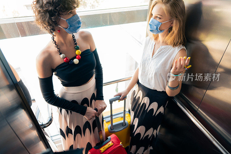 新冠肺炎疫情期间，戴着防护口罩的女性在电梯里聊天