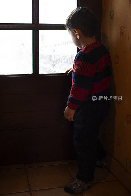 一个小男孩站在窗前望着窗外