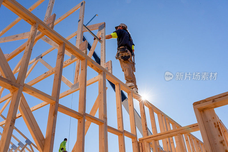 一个构架师站在一个新房屋建筑的骨架墙上，指导起重机操作员安装另一个桁架