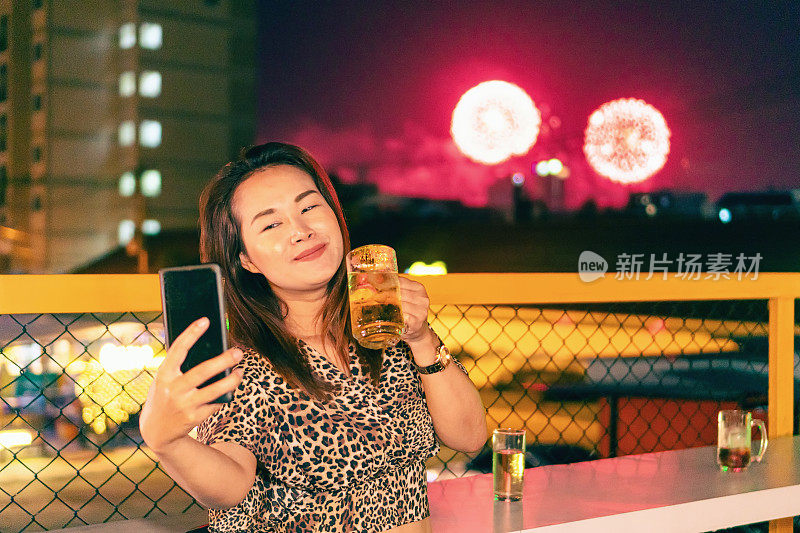 亚洲女人在烟花背景下喝着啤酒自拍