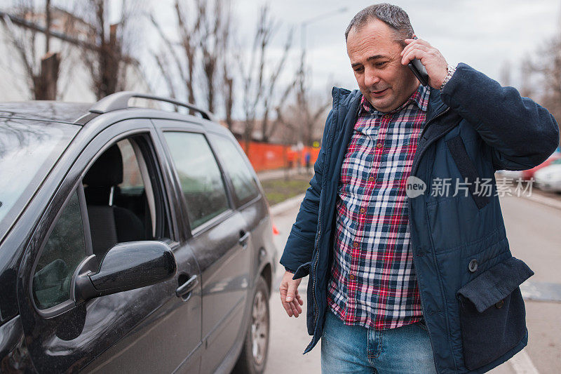 一名男子站在一辆车旁，通过智能手机交谈