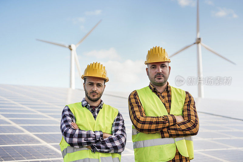在太阳能发电站的工人看起来严肃的相机-太阳能板与风力涡轮机的背景-绿色能源的可再生概念