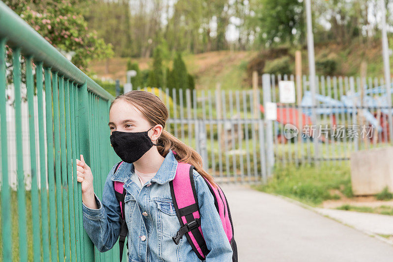 一名戴着口罩的女学生在校门外等待新冠肺炎疫情封锁后重新开放