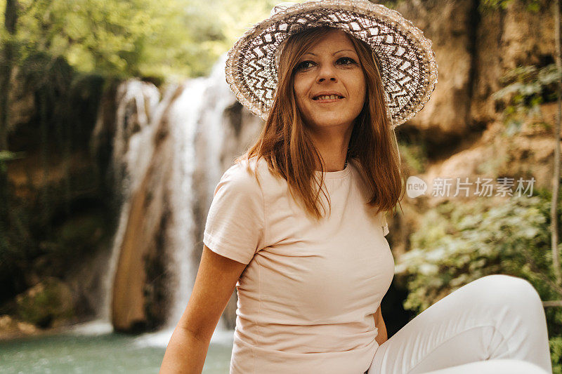 一个美丽的年轻女子，头上戴着一顶帽子，坐在瀑布旁边