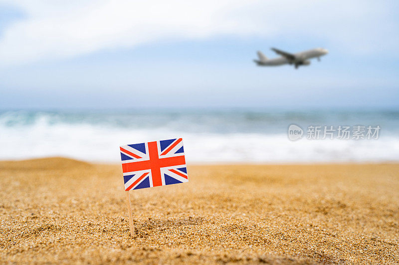 英国国旗以牙签的形式出现在沙滩对面，海浪带着飞机降落。旅游的概念