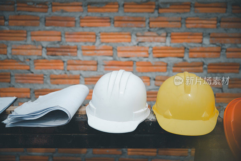 安全帽(安全帽)，图纸，图纸(供工程师，安全员或建筑师使用)，放置在木地板，砖背景上。施工现场佩戴橙色和白色安全帽。
