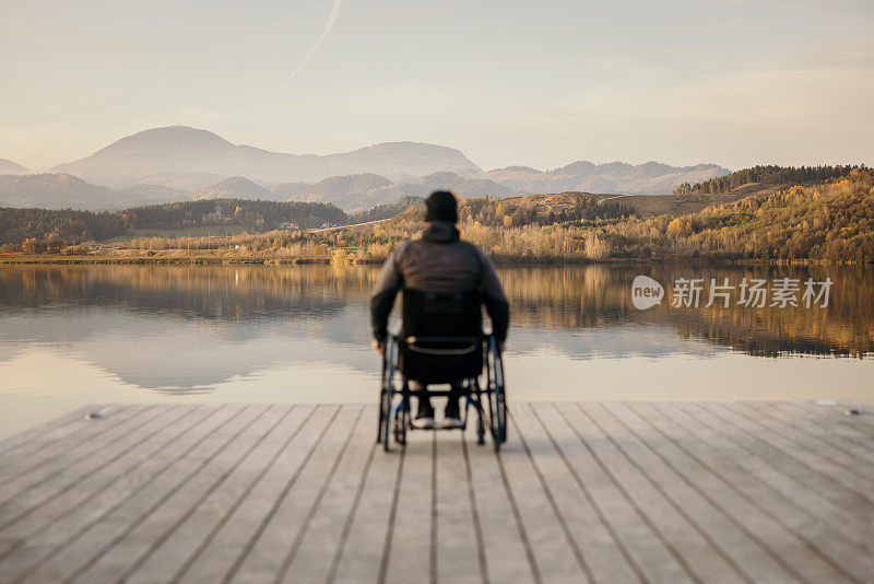 残疾人坐在轮椅上，在码头上欣赏着湖边的自然风光