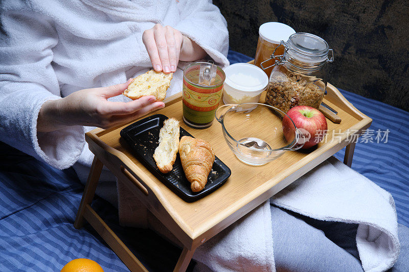 成熟的女人穿着浴衣和睡衣坐在床前吃早餐