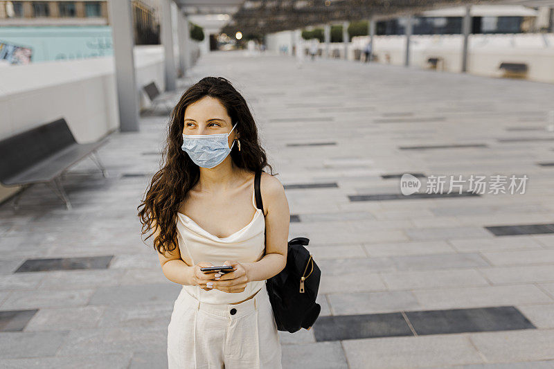 冠状病毒大流行期间，快乐的女人在街上使用智能手机