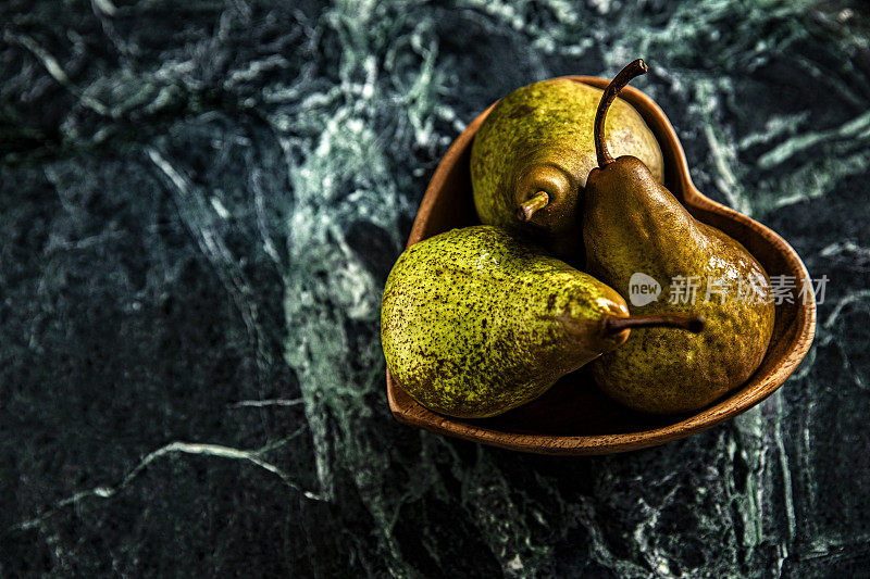 这是一张忧郁的照片，三个梨在一个心碗里，大理石绿色的背景