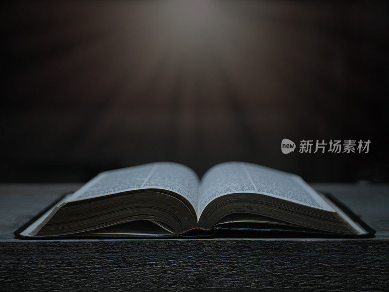 在木桌上打开《圣经》，光线从上方照射过来。(教会概念。)