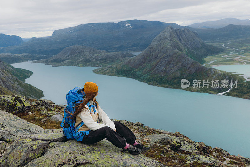 挪威约顿海门国家公园，一名女背包客坐在山顶上凝视着群山的侧视图