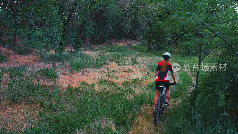 一个戴头盔的女人沿着森林里的小路骑着自行车