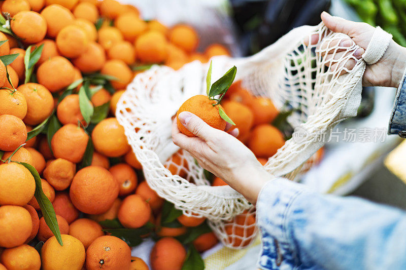 年轻的成年妇女用可重复使用的袋子在市场上买橘子