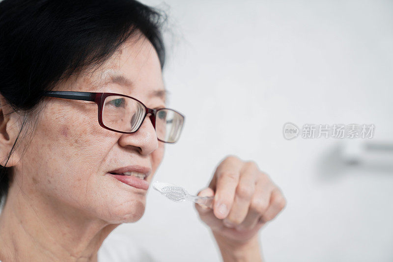亚洲老年妇女在家庭浴室刷牙。