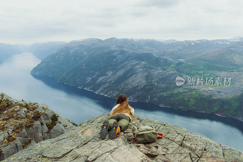 背着背包的女人在悬崖边放松，欣赏挪威吕瑟峡湾田园诗般的景色