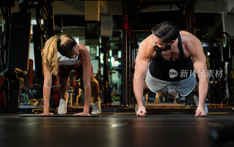 一对运动肌肉男男女女一起做全平板支撑，在现代健身房进行强有力的锻炼