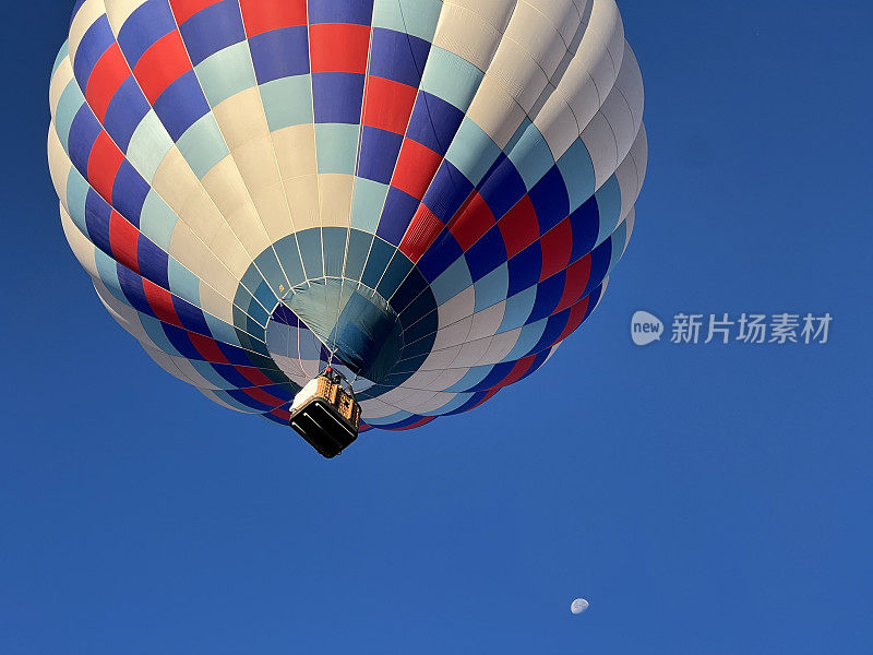 近距离拍摄的热气球在空中滑翔，下方有半个月亮