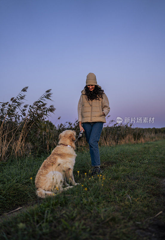 一名女子带着金毛猎犬在湖边和芦苇边的草地上放松