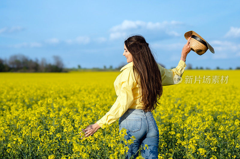 美丽的年轻女子在油菜籽地里享受着无忧无虑的春日