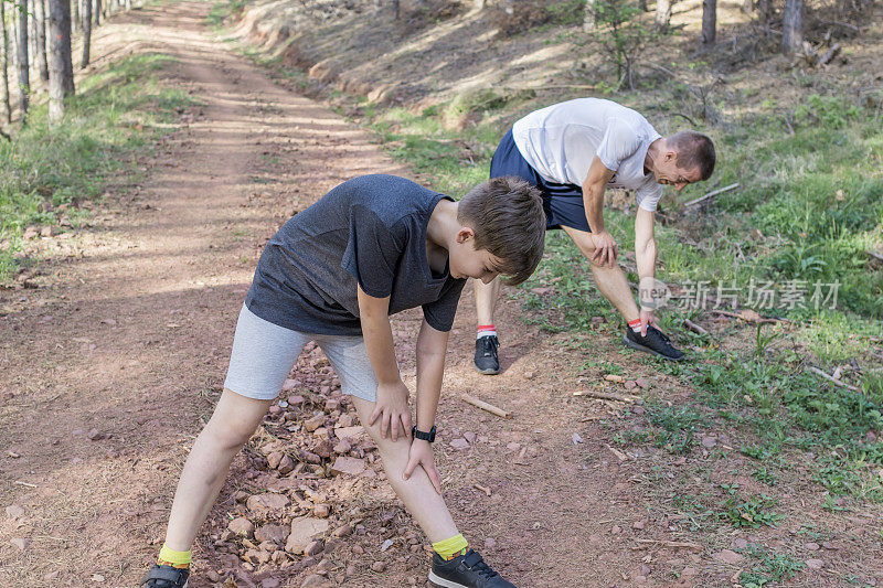 快乐的父亲和儿子正在森林里跑步和锻炼。他们在外面伸伸懒腰，一起享受。运动的生活方式。