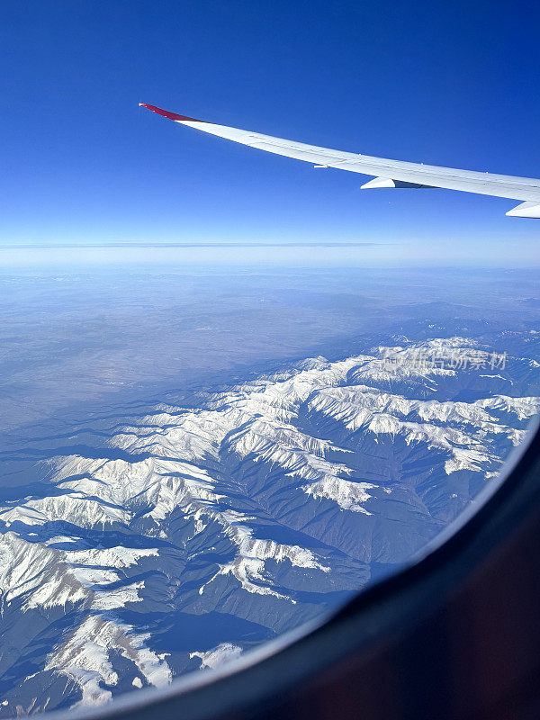 从飞机窗口观看的图像，飞机机翼看到山脉景观，雪山，蓝天，鸟瞰图，小翼和板条，重点在前景