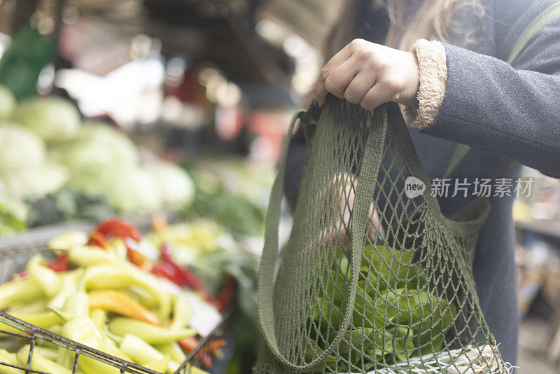 买完新鲜蔬菜后，这位女士把杂货放在一个可重复使用的网袋里