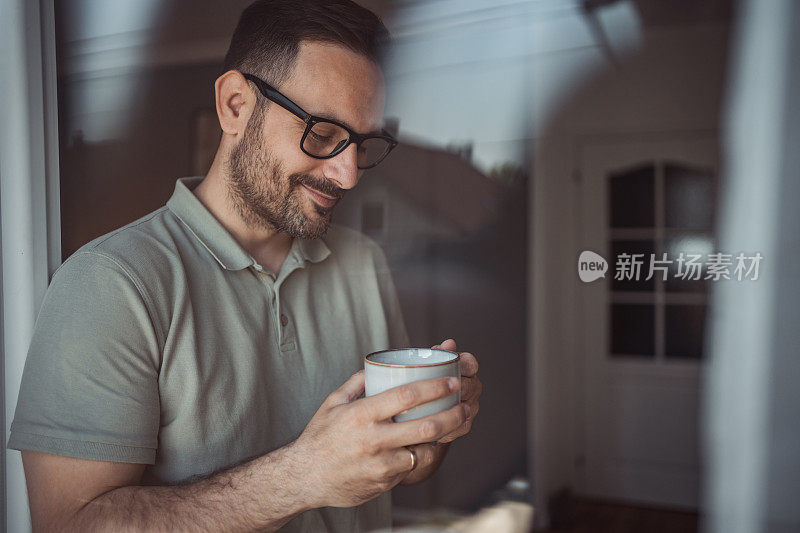 一位成年男子端着一杯咖啡，面带微笑地站在公寓的阳台门口