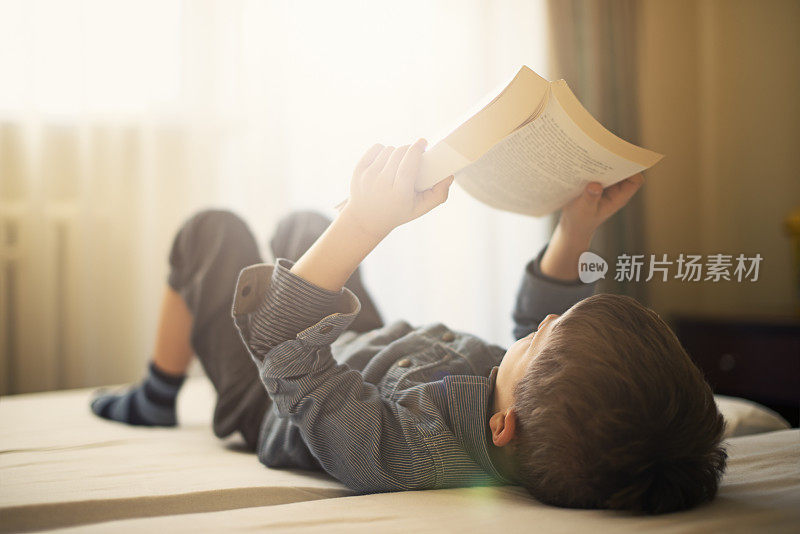 小男孩躺在床上看书