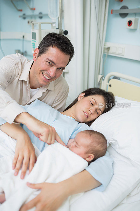 快乐的父亲看着他的妻子和刚出生的婴儿睡觉