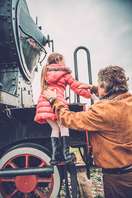 可爱的女孩在爷爷的帮助下从老式蒸汽机车上爬起来