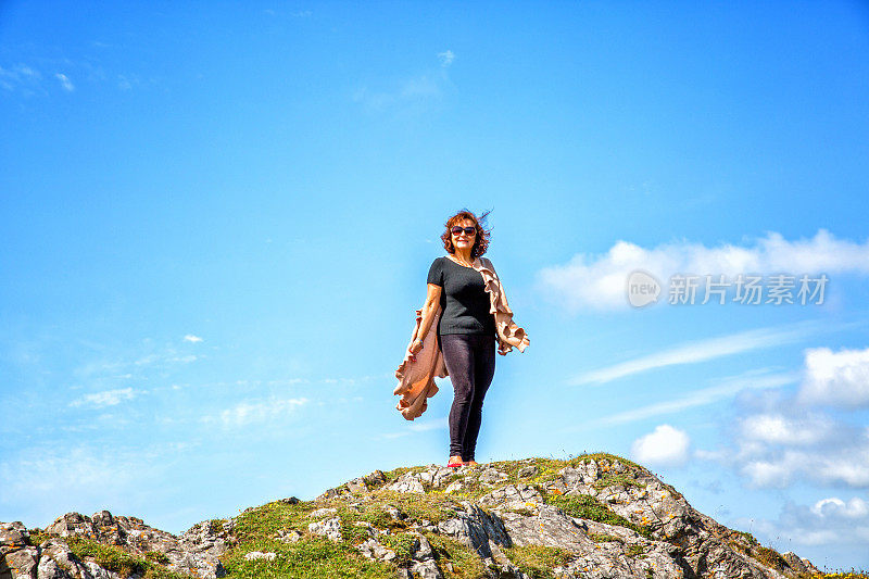 一个成熟的西班牙女人站在遥远的海岸岬角上