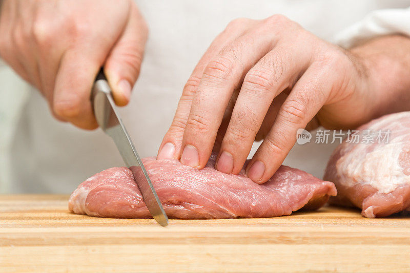 厨师的手拿着刀在厨房的木板上切着一块肉。准备做饭。食品的概念。